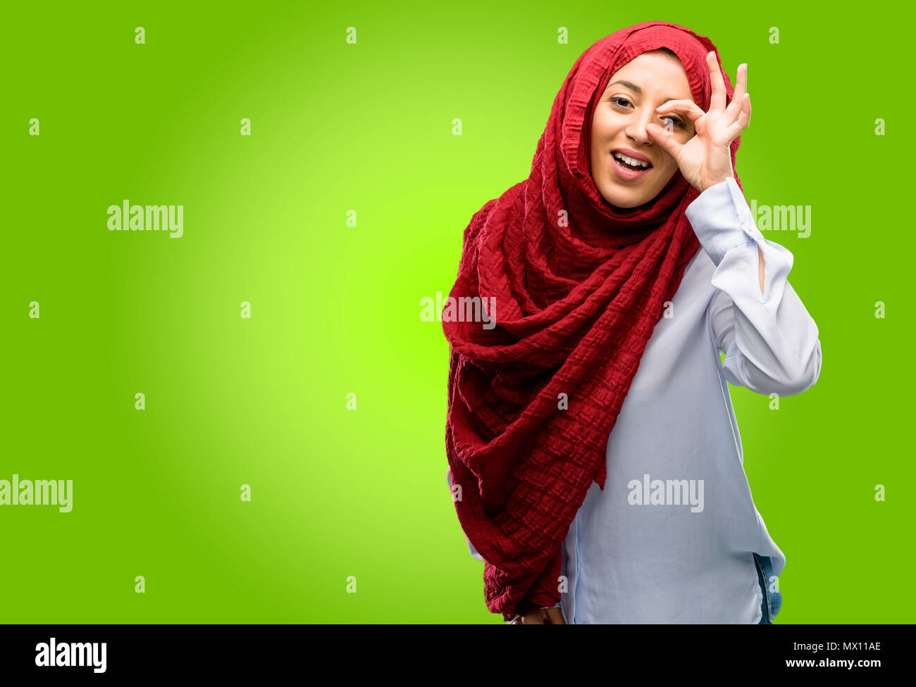young-arab-woman-wearing-hijab-looking-at-camera-through-her-fingers-in-ok-gesture-imitating-binoculars-beautiful-eyes-and-smile-MX11AE.jpg