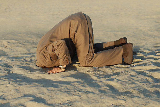 businessman-with-head-stuck-in-sand-at-the-beach-picture-id92655990